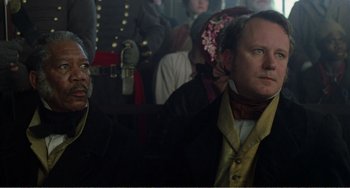 Movie still from “Amistad” (1997), directed by Steven Spielberg – A man in a black jacket is sitting next to another man in a black jacket; Close Up shot, Over the shoulder angle