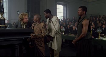 Movie still from “Amistad” (1997), directed by Steven Spielberg – A group of people standing around a room; Wide shot, Over the shoulder angle