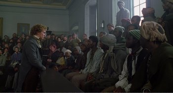 Movie still from “Amistad” (1997), directed by Steven Spielberg – A group of people sitting in a room with a man standing in front of them; Wide shot, High angle