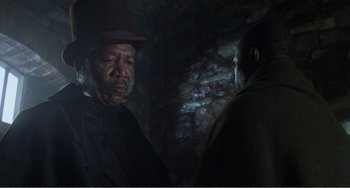 Movie still from “Amistad” (1997), directed by Steven Spielberg – A man in a top hat and a man with a beard in a dark cave; Close Up shot, Over the shoulder angle