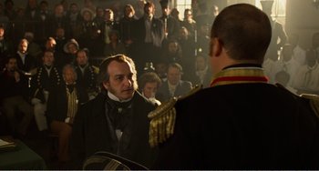 Movie still from “Amistad” (1997), directed by Steven Spielberg – A man in a suit and tie standing in front of a group of people; Medium shot, Over the shoulder angle