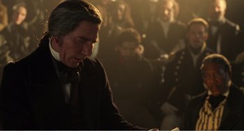 Movie still from “Amistad” (1997), directed by Steven Spielberg – A man in a suit and bow tie looking down at papers; Medium shot, Over the shoulder angle
