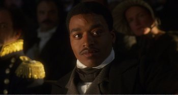 Movie still from “Amistad” (1997), directed by Steven Spielberg – A man in a suit and tie looking at the camera; Close Up shot, High angle