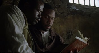 Movie still from “Amistad” (1997), directed by Steven Spielberg – A couple of men sitting next to each other looking at a book; Close Up shot, High angle
