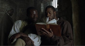 Movie still from “Amistad” (1997), directed by Steven Spielberg – A couple of men sitting next to each other reading a book; Medium shot, High angle