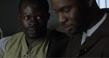 Movie still from “Amistad” (1997), directed by Steven Spielberg – Two black men looking at each other in a dark room; Close Up shot, Over the shoulder angle