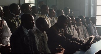 Movie still from “Amistad” (1997), directed by Steven Spielberg – A group of men sitting next to each other in front of a window; Medium shot, High angle
