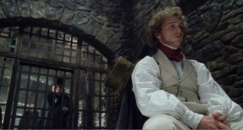 Movie still from “Amistad” (1997), directed by Steven Spielberg – A man sitting in front of a stone wall; Medium shot, Low angle
