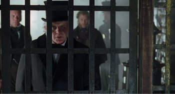 Movie still from “Amistad” (1997), directed by Steven Spielberg – A man wearing a top hat looking through a jail cell; Medium shot, Low angle