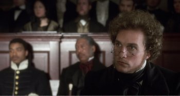 Movie still from “Amistad” (1997), directed by Steven Spielberg – A man in a black coat and glasses in a courtroom; Close Up shot, High angle