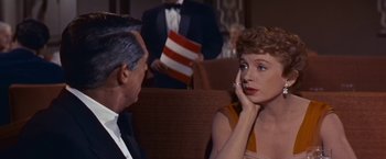 Movie still from “An Affair to Remember” (1957), directed by Leo McCarey – A woman sitting in a chair with a man in the background; Medium shot, Over the shoulder angle