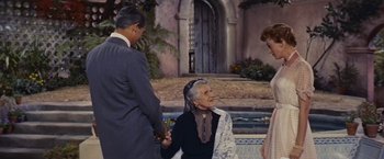 Movie still from “An Affair to Remember” (1957), directed by Leo McCarey – An older woman wearing a black dress holding hands with two other people; Medium shot, Over the shoulder angle