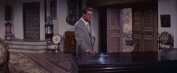 Movie still from “An Affair to Remember” (1957), directed by Leo McCarey – A man in a gray suit standing in front of a table; Medium shot, High angle