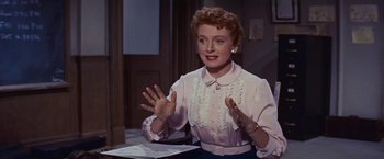 Movie still from “An Affair to Remember” (1957), directed by Leo McCarey – An older woman is sitting at a table with her hands raised; Medium shot, Low angle