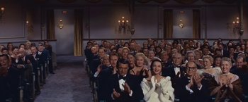 Movie still from “An Affair to Remember” (1957), directed by Leo McCarey – A group of people sitting in a room clapping; Wide shot, High angle