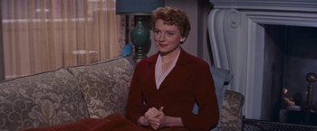 Movie still from “An Affair to Remember” (1957), directed by Leo McCarey – A woman sitting on top of a couch in front of a lamp; Medium shot, High angle