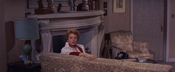 Movie still from “An Affair to Remember” (1957), directed by Leo McCarey – A woman sitting on top of a couch in front of a fireplace; Medium shot, High angle