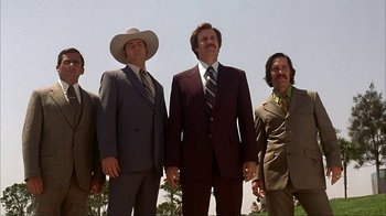 Movie still from “Anchorman: The Legend of Ron Burgundy” (2004), directed by Adam McKay – A group of men standing next to each other in suits; Wide shot, Low angle