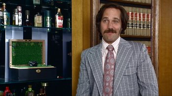 Movie still from “Anchorman: The Legend of Ron Burgundy” (2004), directed by Adam McKay – A man in a suit and tie standing in front of a bookshelf; Medium shot, Low angle