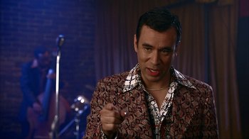 Movie still from “Anchorman: The Legend of Ron Burgundy” (2004), directed by Adam McKay – A man in a brown and white shirt and a microphone; Medium shot, Over the shoulder angle