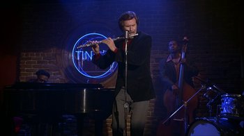 Movie still from “Anchorman: The Legend of Ron Burgundy” (2004), directed by Adam McKay – A man playing a flute in front of a microphone; Wide shot, Low angle