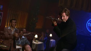 Movie still from “Anchorman: The Legend of Ron Burgundy” (2004), directed by Adam McKay – A man playing the flute in front of a group of people; Medium shot, Low angle