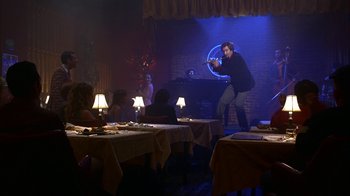 Movie still from “Anchorman: The Legend of Ron Burgundy” (2004), directed by Adam McKay – A man standing in front of a table in a room; Wide shot, Over the shoulder angle