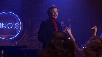 Movie still from “Anchorman: The Legend of Ron Burgundy” (2004), directed by Adam McKay – A man in a black jacket and red shirt standing in front of a brick wall; Medium shot, Over the shoulder angle