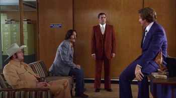 Movie still from “Anchorman: The Legend of Ron Burgundy” (2004), directed by Adam McKay – A man in a red suit standing next to another man in a gray suit; Wide shot, Low angle