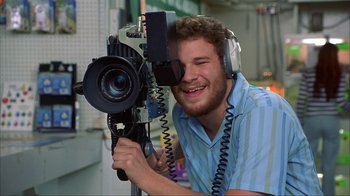 Movie still from “Anchorman: The Legend of Ron Burgundy” (2004), directed by Adam McKay – A man with headphones on holding up a camera; Close Up shot, Over the shoulder angle