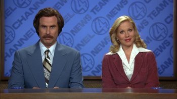 Movie still from “Anchorman: The Legend of Ron Burgundy” (2004), directed by Adam McKay – Two anchorman characters sitting at a news desk; Medium shot, Low angle