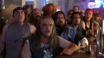 Movie still from “Anchorman: The Legend of Ron Burgundy” (2004), directed by Adam McKay – A group of men sitting at a table with a bottle of beer; Medium shot, Low angle