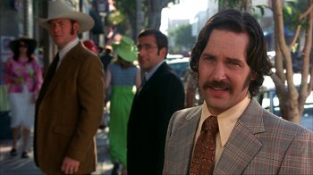 Movie still from “Anchorman: The Legend of Ron Burgundy” (2004), directed by Adam McKay – A man in a suit and tie standing in front of other men; Close Up shot, Over the shoulder angle