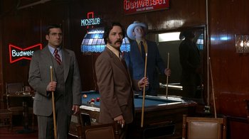 Movie still from “Anchorman: The Legend of Ron Burgundy” (2004), directed by Adam McKay – A group of men standing around a billiards table; Medium shot, Low angle