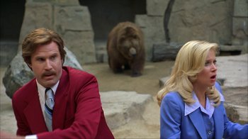 Movie still from “Anchorman: The Legend of Ron Burgundy” (2004), directed by Adam McKay – A man and a woman sitting next to each other in front of a bear; Medium shot, Over the shoulder angle