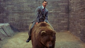 Movie still from “Anchorman: The Legend of Ron Burgundy” (2004), directed by Adam McKay – A man in a suit riding on the back of a brown bear; Wide shot, Low angle