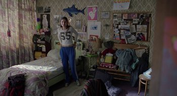 Movie still from “And Your Mother Too” (2001), directed by Alfonso Cuarón – A woman standing in a room with a lot of pictures on the wall; Wide shot, Over the shoulder angle