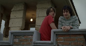 Movie still from “And Your Mother Too” (2001), directed by Alfonso Cuarón – Two young men are sitting on a brick wall; Medium shot, Low angle