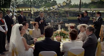 Movie still from “And Your Mother Too” (2001), directed by Alfonso Cuarón – A group of people sitting around a table at an outdoor event; Wide shot, Over the shoulder angle