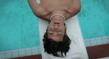 Movie still from “And Your Mother Too” (2001), directed by Alfonso Cuarón – A man laying on a towel near a swimming pool; Close Up shot, Overhead angle