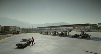 Movie still from “And Your Mother Too” (2001), directed by Alfonso Cuarón – A man standing in front of a gas station with cars; Extreme Wide shot, High angle