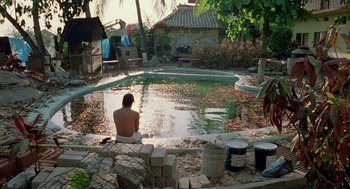 Movie still from “And Your Mother Too” (2001), directed by Alfonso Cuarón – A person sitting in front of a pool of water; Wide shot, High angle