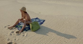 Movie still from “And Your Mother Too” (2001), directed by Alfonso Cuarón – A woman sitting on a towel on the beach; Wide shot, Overhead angle