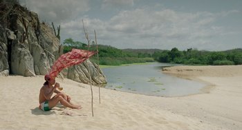 Movie still from “And Your Mother Too” (2001), directed by Alfonso Cuarón – A woman sitting on the beach under an umbrella; Extreme Wide shot, High angle
