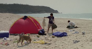 Movie still from “And Your Mother Too” (2001), directed by Alfonso Cuarón – A man and a dog on the beach near a tent; Wide shot, High angle