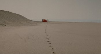 Movie still from “And Your Mother Too” (2001), directed by Alfonso Cuarón – Two people standing on the beach near a red tent; Extreme Wide shot, High angle