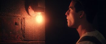Movie still from “Angel of Anywhere” (2018), directed by James Kicklighter – A man looking at a light bulb in a dark room; Close Up shot, Low angle