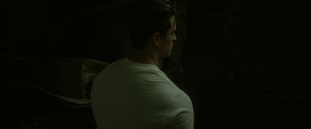 Movie still from “Angel of Anywhere” (2018), directed by James Kicklighter – A man in a white shirt is standing in a dark room; Medium shot, Low angle