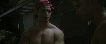 Movie still from “Angel of Anywhere” (2018), directed by James Kicklighter – A shirtless man wearing a red hat in a dark room; Close Up shot, Over the shoulder angle