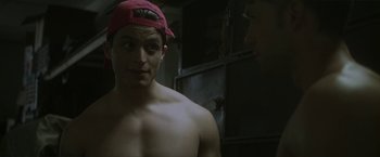 Movie still from “Angel of Anywhere” (2018), directed by James Kicklighter – A shirtless man wearing a red hat in a dark room; Close Up shot, Over the shoulder angle